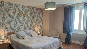 A bedroom with a bed, a chair, a lamp, a window with curtains, and a wall with a leaf pattern. - Le gîte du Vigneron - LABASTIDE-DE-LEVIS (LABASTIDE-DE-LEVIS)