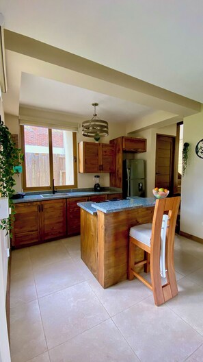 Una cocina con armarios de madera, una isla integrada con un lavamanos, un refrigerador y una araña.