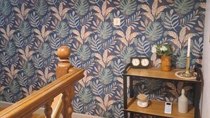 A room with a patterned wallpaper, a wooden staircase, a shelf with decorative items, and an air conditioning unit. - Lou Tinalou - CASTRES (CASTRES)