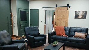 A living room with two black leather sofas, a coffee table with a plant, and a green door.