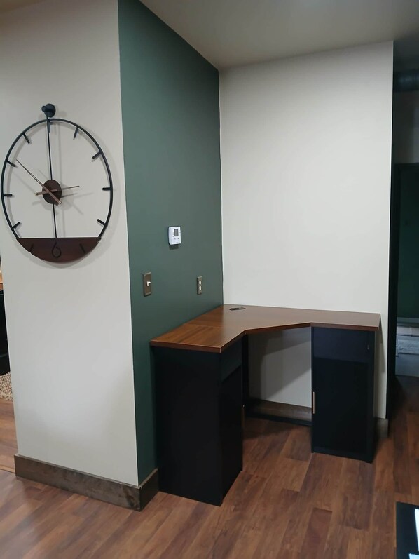 Une pièce avec un bureau en bois, une horloge murale et un thermostat.