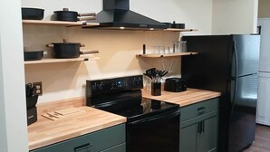 A compact kitchen with a black stove, a black refrigerator, and wooden shelves.