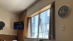 Une chambre d’hôtel dotée d’une grande fenêtre, d’une horloge murale, d’un téléviseur à écran plat et d’une table de chevet agrémentée d’une plante.