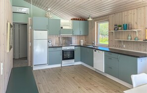 Una cocina moderna con armarios verde claro, una estufa de acero inoxidable y un ventanal con vistas a la vegetación.