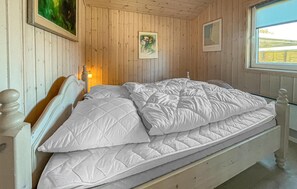Ein Bett in einem Zimmer mit Holzwänden, einem gerahmten Bild an der Wand und einem Fenster.