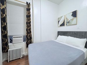 Une chambre à coucher comprenant un lit, un radiateur, une fenêtre avec des stores et deux œuvres d’art accrochées au mur.