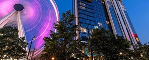 Una noria con una exhibición de luces moradas, rodeada de edificios modernos y árboles.