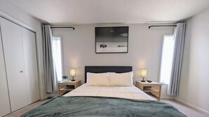 A neatly arranged bedroom with a bed, two bedside tables with lamps, a large window with curtains, and a framed picture on the wall. - Charming 3-bedroom house CLOSE TO STADIUM - Manhattan (Manhattan)