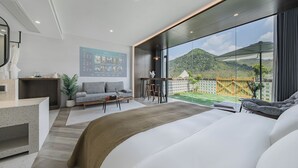 A modern hotel room with a large bed, a seating area with a sofa and chairs, a small desk, and a large window offering a view of the outdoors. - Qingcen Manor (Huzhou)