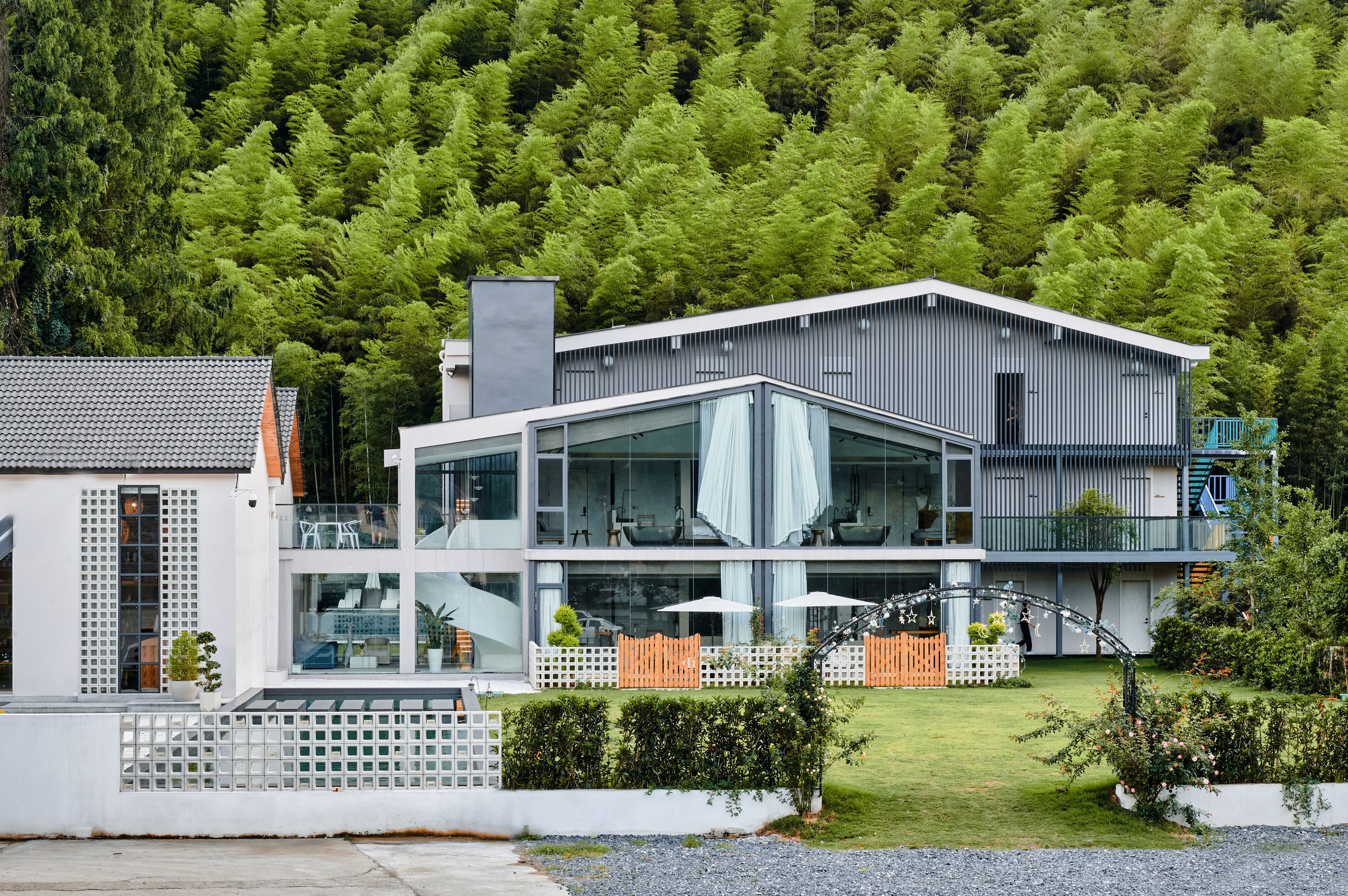 A modern two-story house with large glass windows, a balcony, and a well-maintained garden.