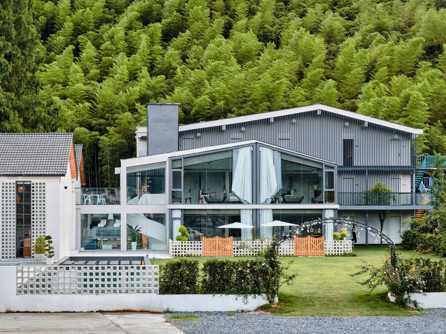 A modern two-story house with large glass windows, a balcony, and a well-maintained garden.