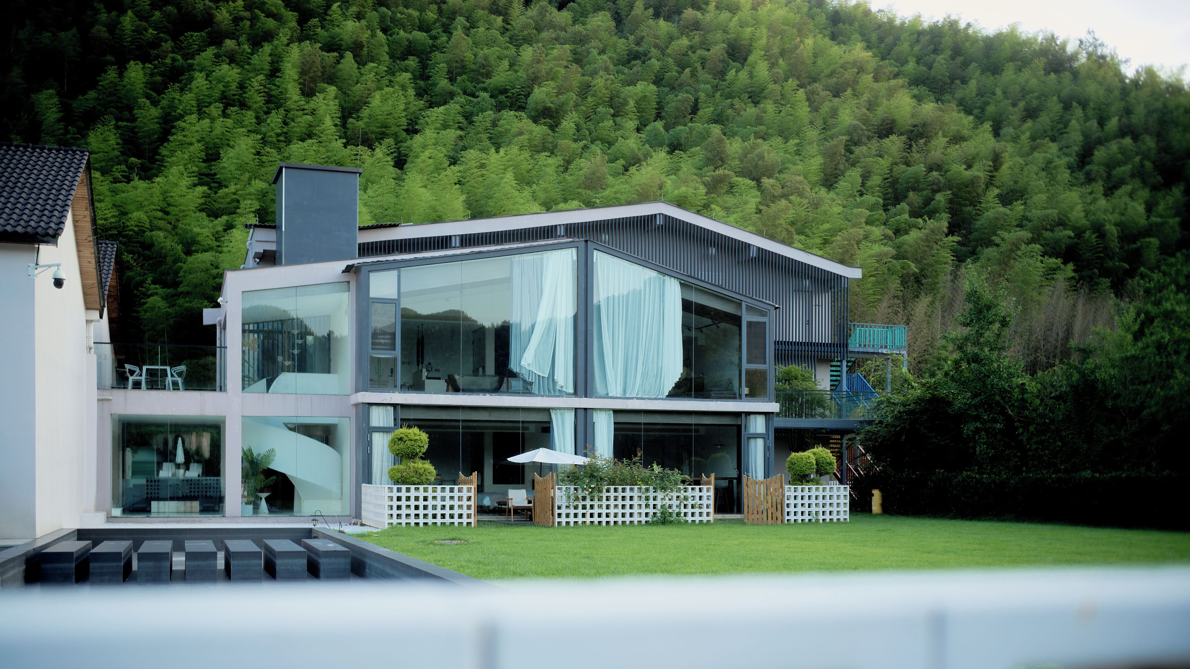 A modern two-story house with large glass windows, a balcony, and a well-maintained garden.