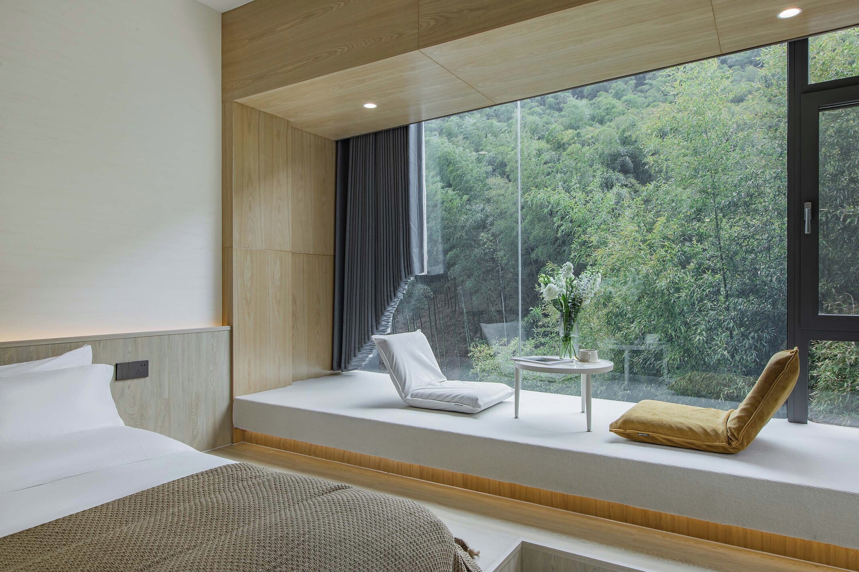 Quarto de hotel moderno com uma janela grande que oferece vista para uma área arborizada.
