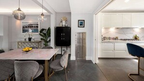 Une cuisine moderne avec des meubles blancs, un four encastré et un coin repas comprenant une table en marbre et des chaises à revêtement gris.