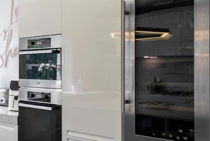Egy konyha beépített sütővel, mikrohullámú sütővel és egy hűtőszekrényjel, amelynek külön fagyasztórekesze van.