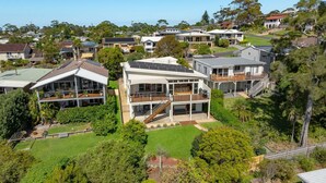 A modern two-story house with a large deck, a covered outdoor area, and a well-maintained lawn. - Aerial Blue Mollymook - Ocean Views, Spacious, Wood Fireplace, Walk to Mollymook Beach & Golf Course (Mollymook)