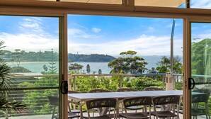 A balcony with a table and chairs, overlooking a coastal landscape with trees and hills. - Aerial Blue Mollymook - Ocean Views, Spacious, Wood Fireplace, Walk to Mollymook Beach & Golf Course (Mollymook)