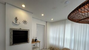 Una sala moderna con chimenea, televisor montado en la pared, mesa de comedor con sillas y un gran ventanal con cortinas.