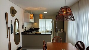 Un comedor con una mesa y sillas de madera, una cocina al fondo y una lámpara de fibra trenzada grande.