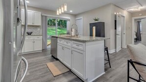 Une cuisine moderne avec des armoires blanches, un grand îlot central et des luminaires suspendus.