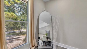 Une pièce dotée d’une grande fenêtre, d’un miroir et donnant sur un parking et des arbres.