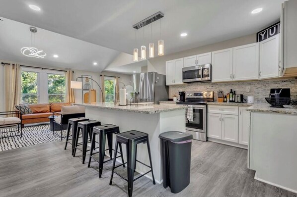 A modern kitchen with white cabinets, stainless steel appliances, and a bar area with stools. - Modern 3 Bedroom/3 Bathroom ATL Retreat! (Atlanta)