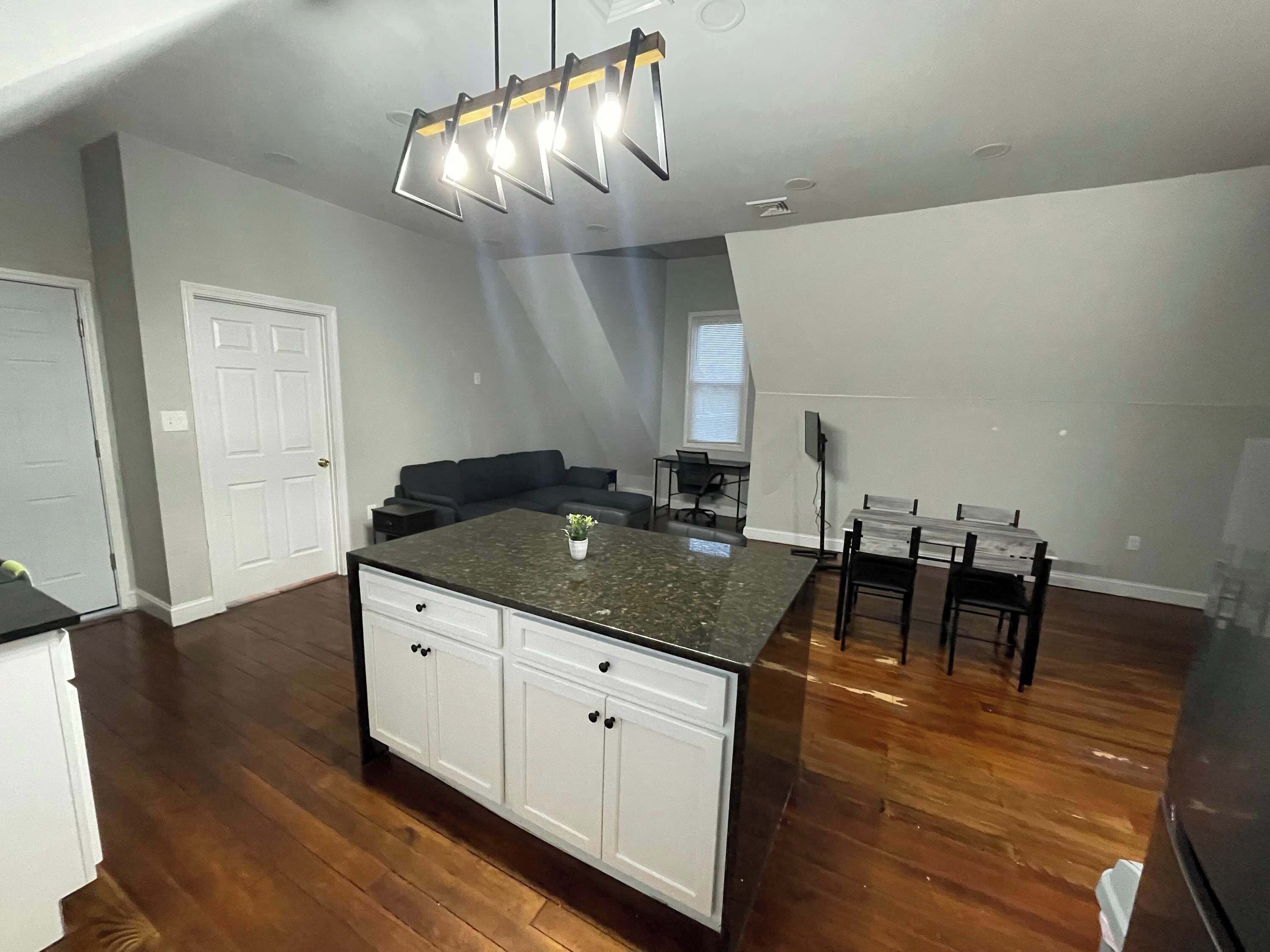 A modern kitchen with a central island, wooden flooring, and a ceiling light fixture.