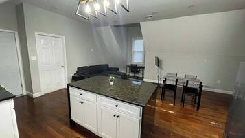 A modern kitchen with a central island, wooden flooring, and a ceiling light fixture.