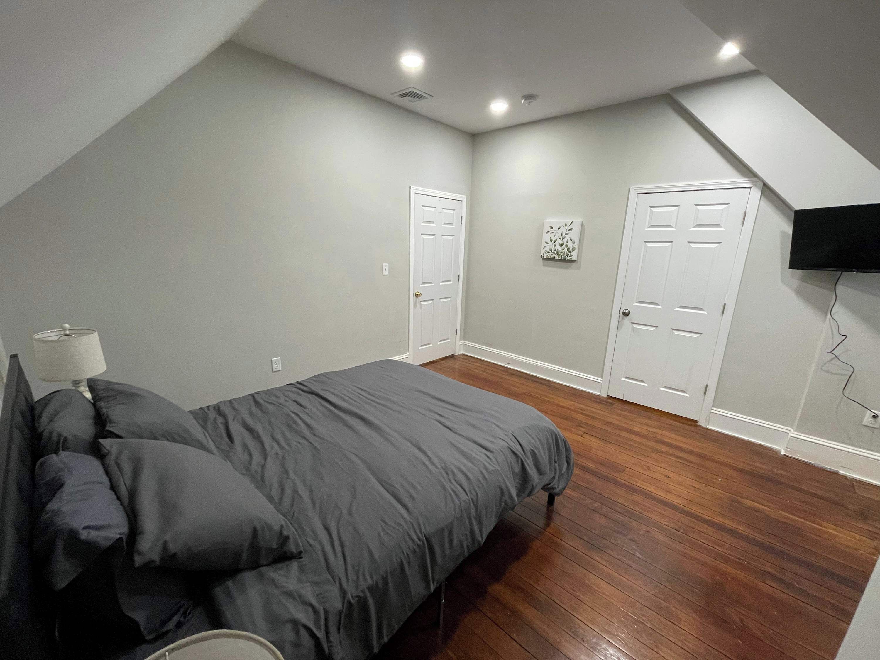 A bedroom with a bed, a nightstand, a lamp, and a TV mounted on the wall.