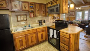 Una cocina con armarios de madera, un refrigerador negro, un microondas y una estufa.