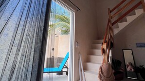 A room with a large sliding glass door leading to a balcony, a wooden staircase, and a small seating area with a blue chair.