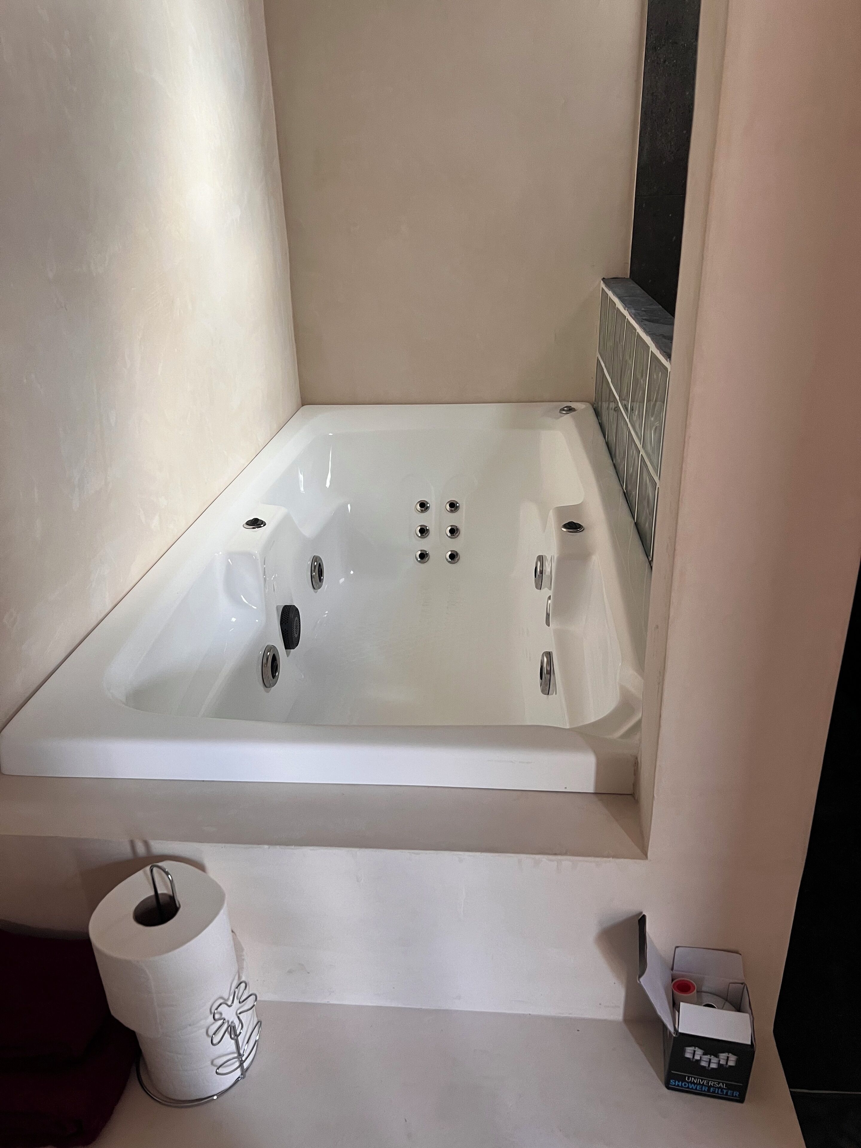 Et badeværelse med et hvidt badekar, toiletpapirholder og en kasse med universal brusefilter.