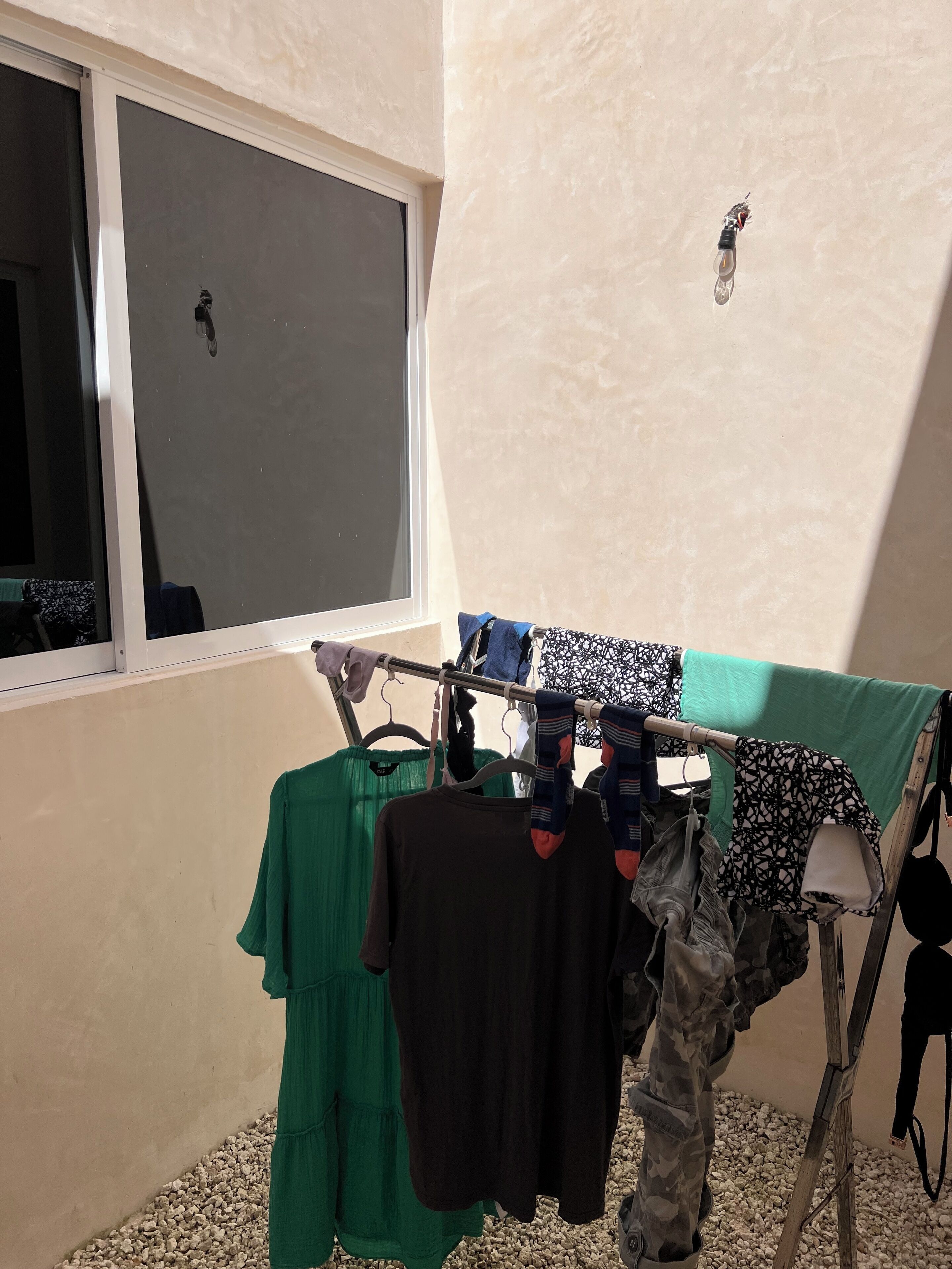 A room with a window, a drying rack with clothes, and a small insect on the wall.