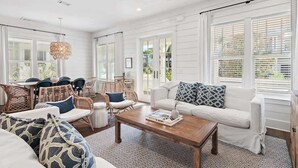 A spacious living room with a white sofa, wicker chairs, a coffee table, and large windows with blinds. - Community pool, 4 Bikes 'Seas the Day' (Santa Rosa Beach)