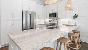 A modern kitchen with white cabinetry, stainless steel appliances, a marble island, wicker bar stools, and woven pendant lights. - Community pool, 4 Bikes 'Seas the Day' (Santa Rosa Beach)