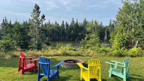 A grassy outdoor area with four Adirondack chairs in red, blue, yellow, and green colors, and a fire pit in the center. - Tidal's Edge Cottage (Fortune Bridge)