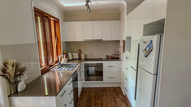 A modern kitchen with white cabinets, a wooden countertop, and a built-in oven. - Sunny Byron Bay House Just 700m from the Beach (Lennox Head)