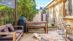 A patio with a wooden table, a barbecue grill, and a sofa. - Sunny Byron Bay House Just 700m from the Beach (Lennox Head)