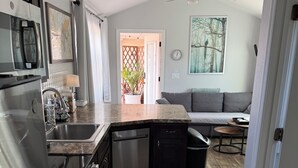A compact kitchen with a dishwasher, a refrigerator, and a microwave. There is a dining area with a sofa and a small table.