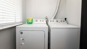 A laundry area with two white front-loading washers and a dryer, a window with blinds, and a hose running to the right. - Cozy Modern 2BR Condo with free Parking (Los Angeles)