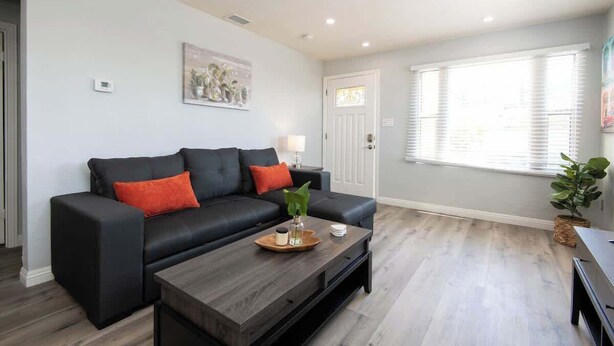 A modern living room with a black leather sofa, a wooden coffee table, and a large window with blinds. - Cozy Modern 2BR Condo with free Parking (Los Angeles)