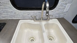 A kitchen sink with a double faucet, a window above, and a tiled backsplash.