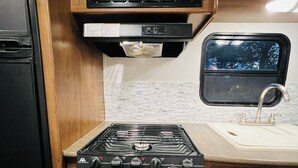 A compact kitchen with a microwave, stove, sink, and a window with a view.