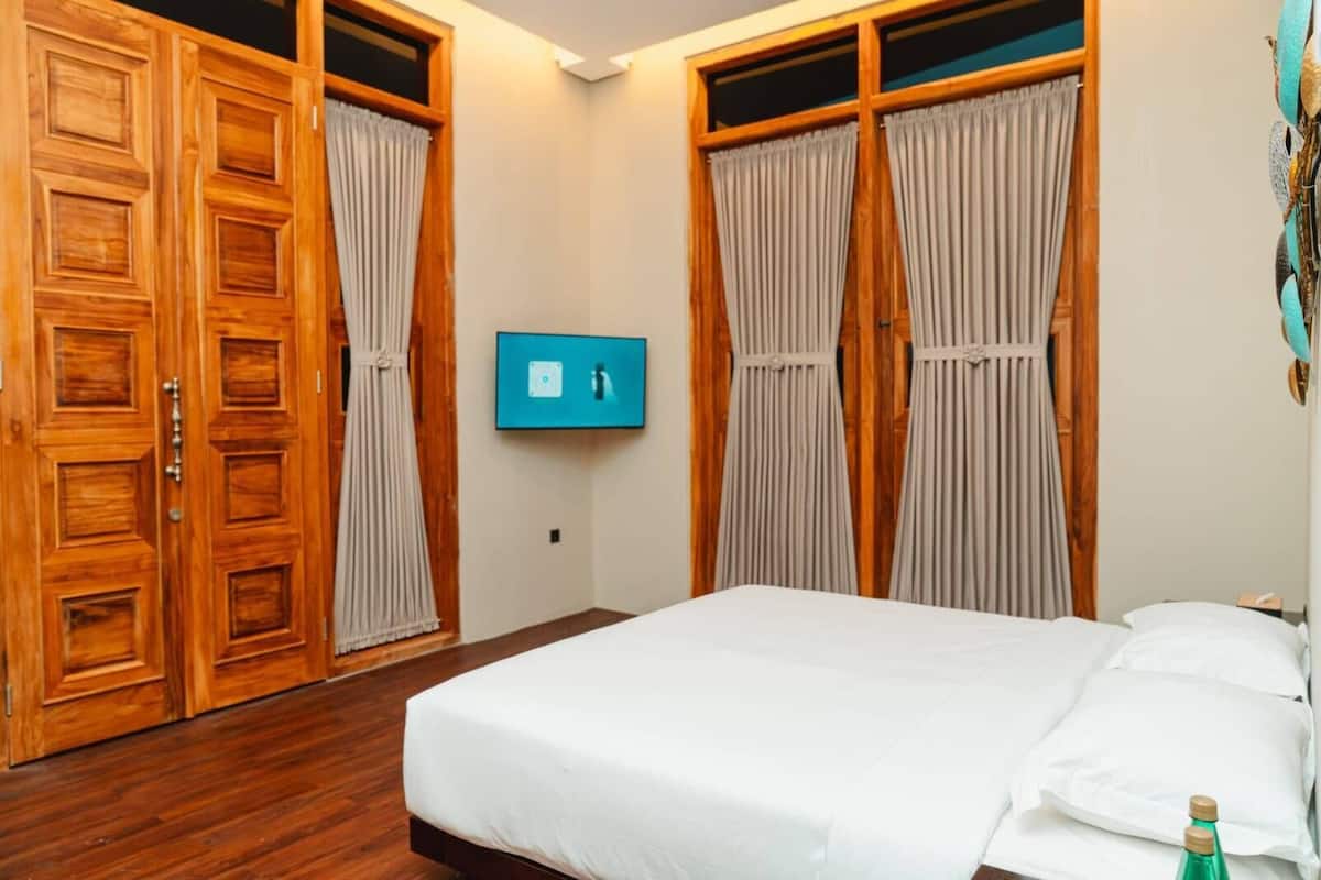 A bedroom with a bed, wooden wardrobe, curtains, a television, and a bottle.