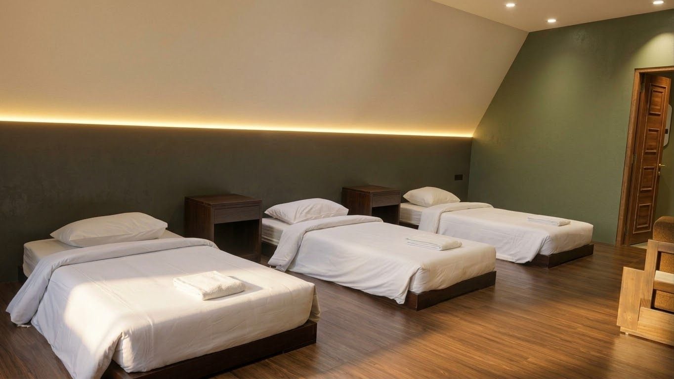 Une chambre d’hôtel avec quatre lits simples, un plancher en bois, un mur d’accent vert et une porte en bois.