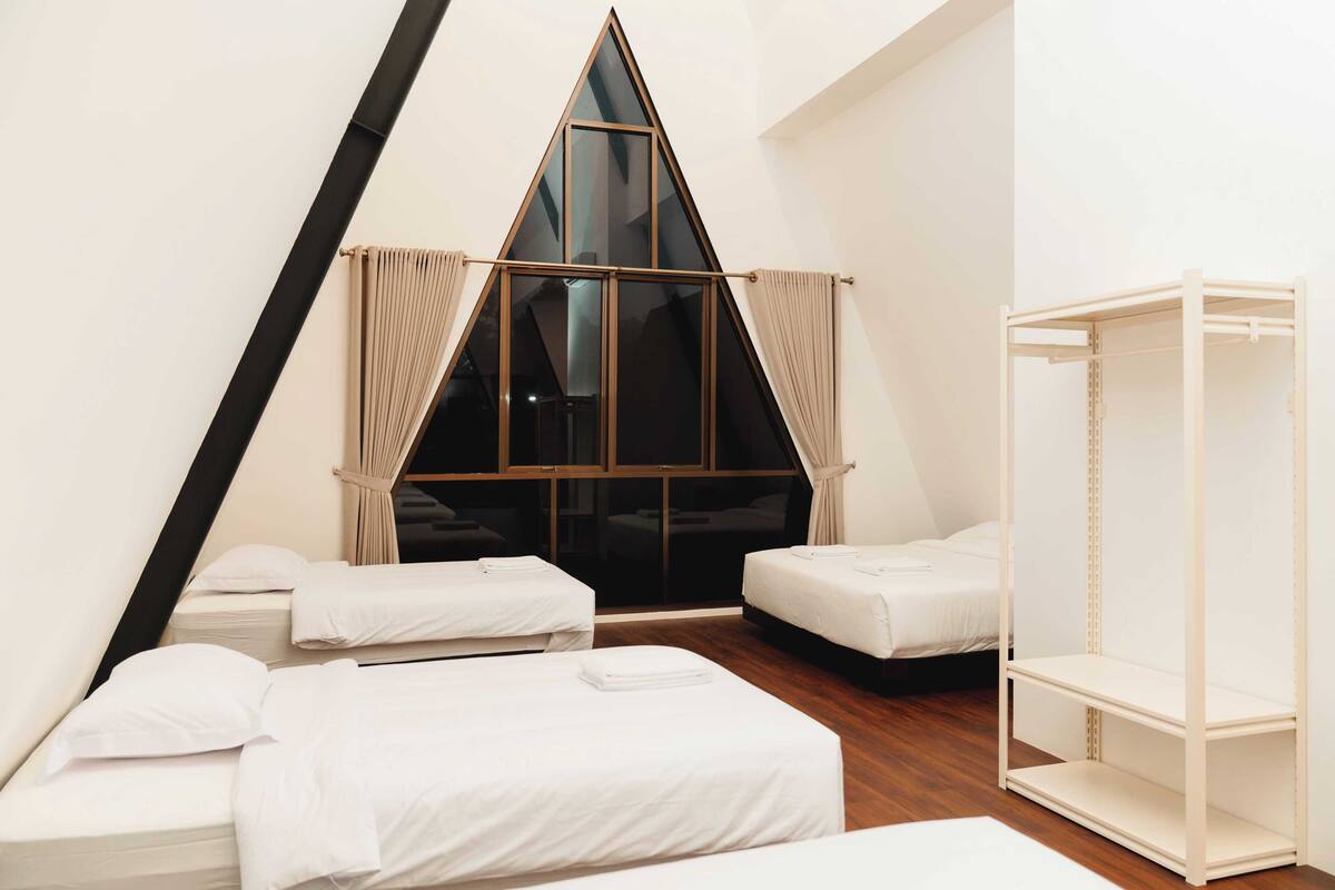 A modern hotel room with a triangular window, two single beds, a small white shelf, and a wooden floor.