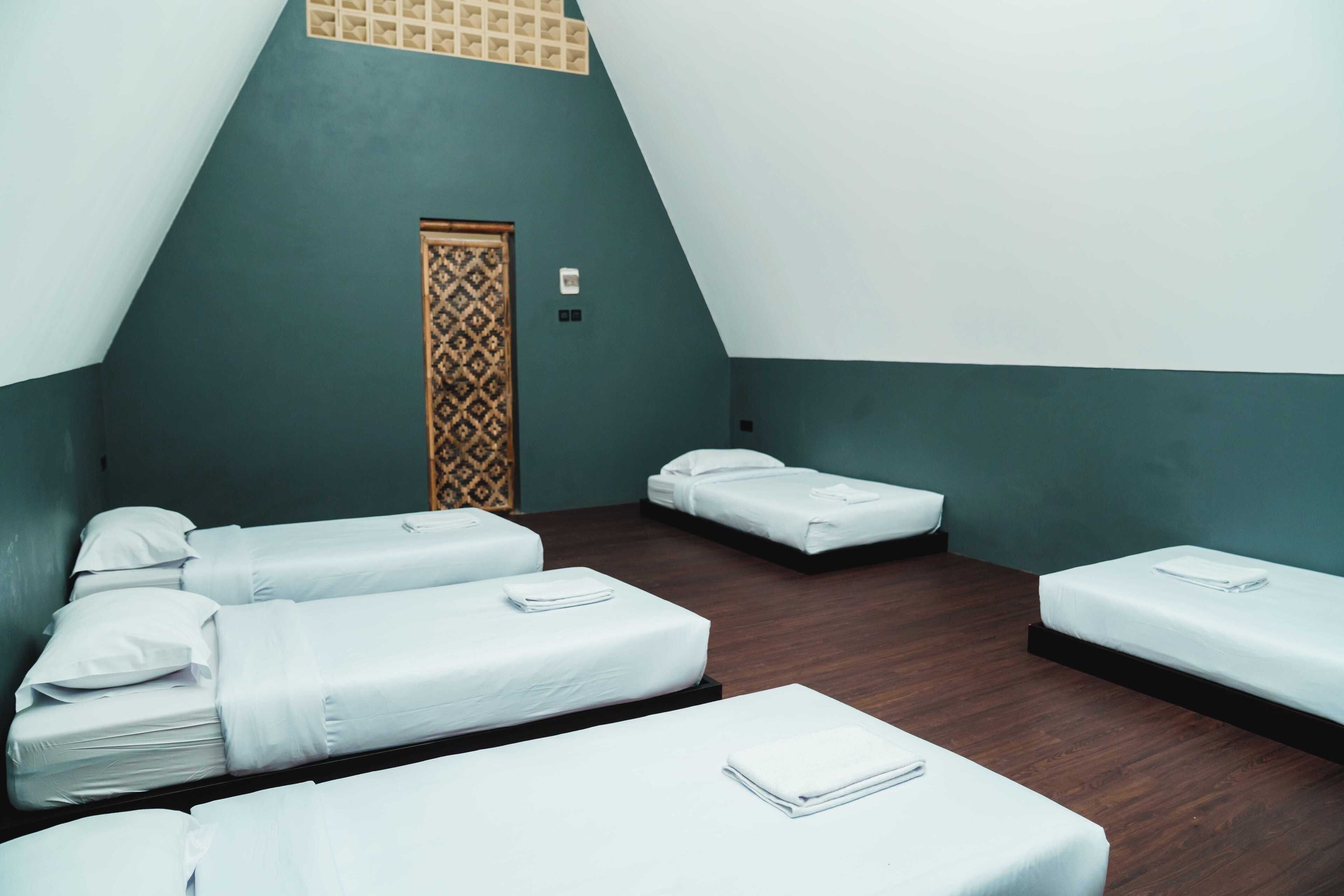 Ein Zimmer mit vier Betten, die in einer U-Form angeordnet sind, einer verzierten Tür und einer hellen Wand.