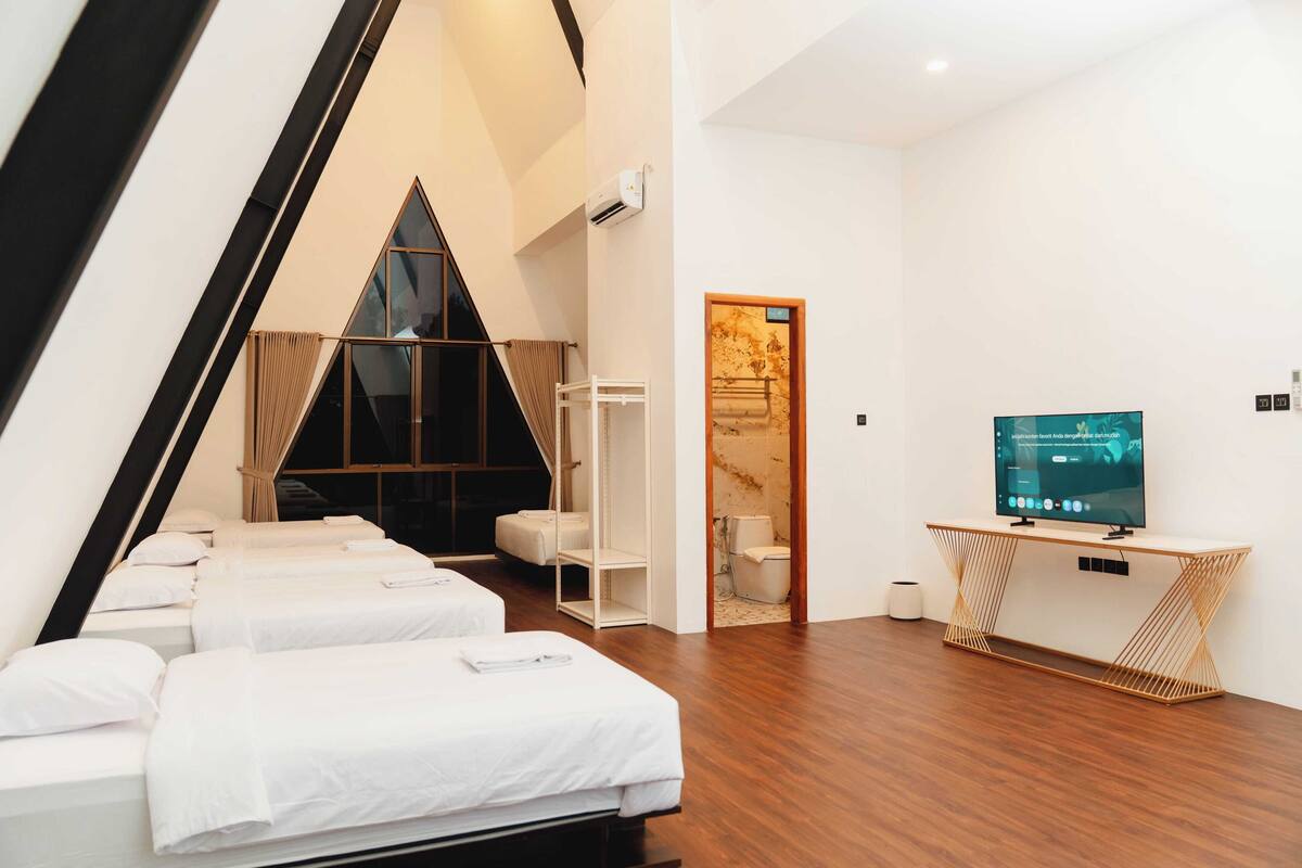 A modern hotel room with a sloped ceiling, two beds, a TV, and a wooden console table.