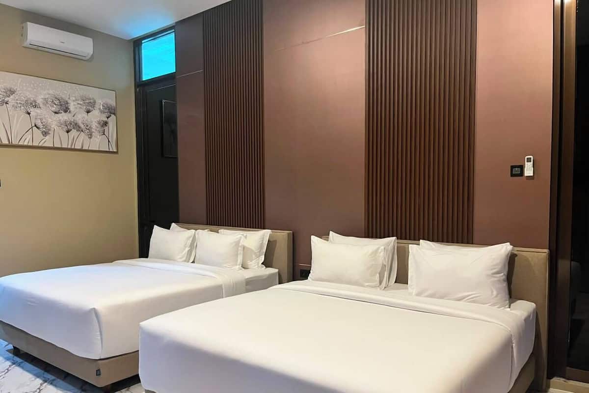 A hotel room with two beds, a marble floor, a wall-mounted air conditioner, and a painting.