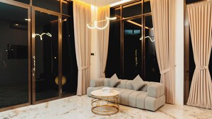 A modern living room with a sofa, a round coffee table, and large windows with curtains. - Acasa Cottage by Samsara (Ciawi)